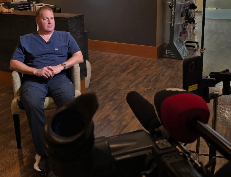 Howard Green sits in his office during an on-camera interview with CBC.  A camera can be seen pointed towards him. 