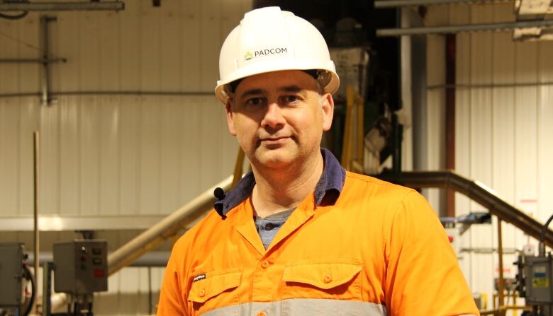 A man in a hard hat and neon orange jacket looks to the camera.