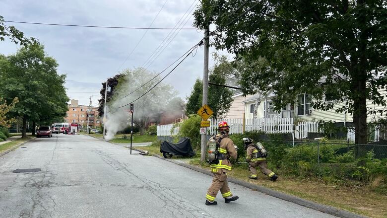 firefighters near smoky pit in pavement near a building.