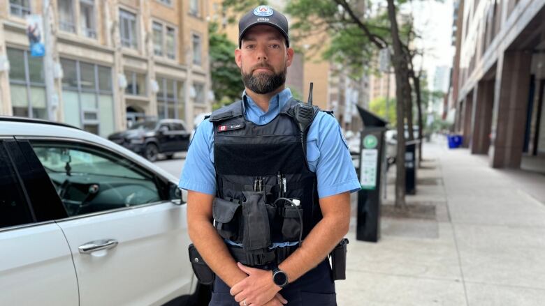 A man in a parking officer uniform stands next to cars on a street.