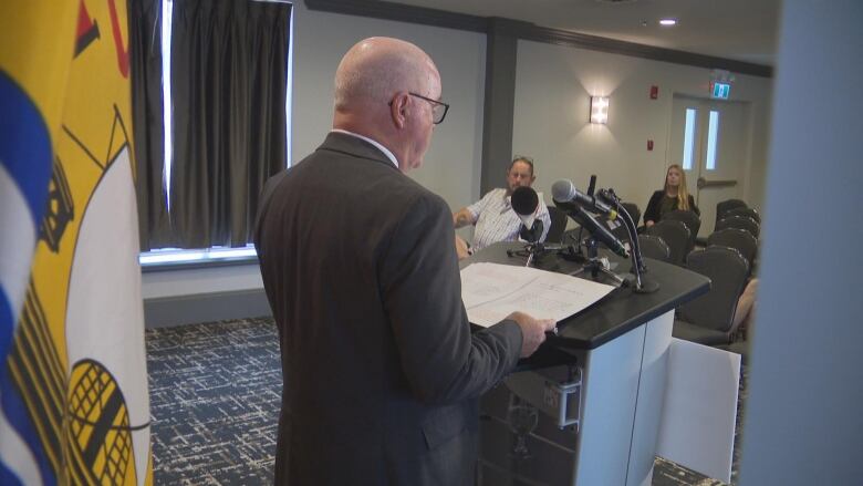 Back of health minister bruce fitch's head as he reads from the podium