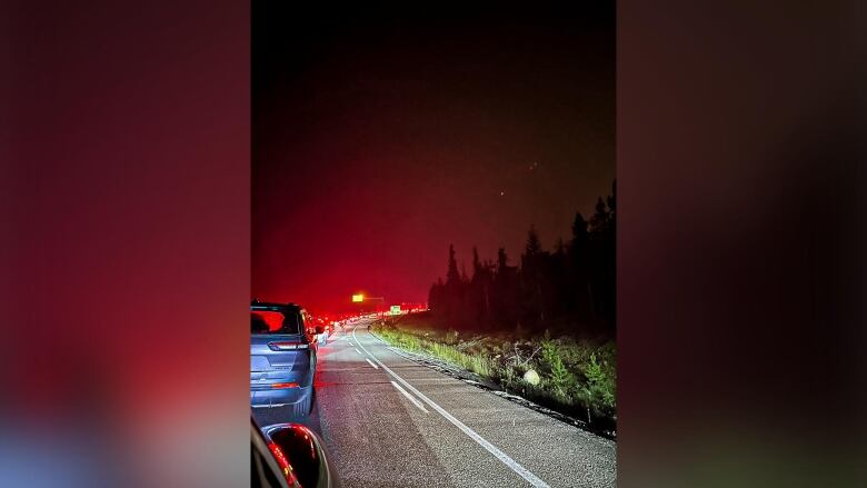 Long line of cars crawling along a highway, at night, with a smoky red sky due to wildfires in the area.