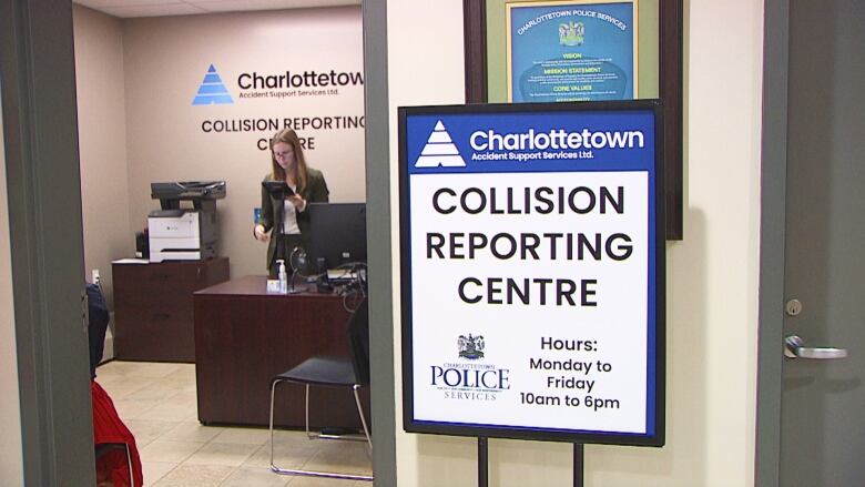 Woman in office with sign outside that says Collision Reporting Centre.