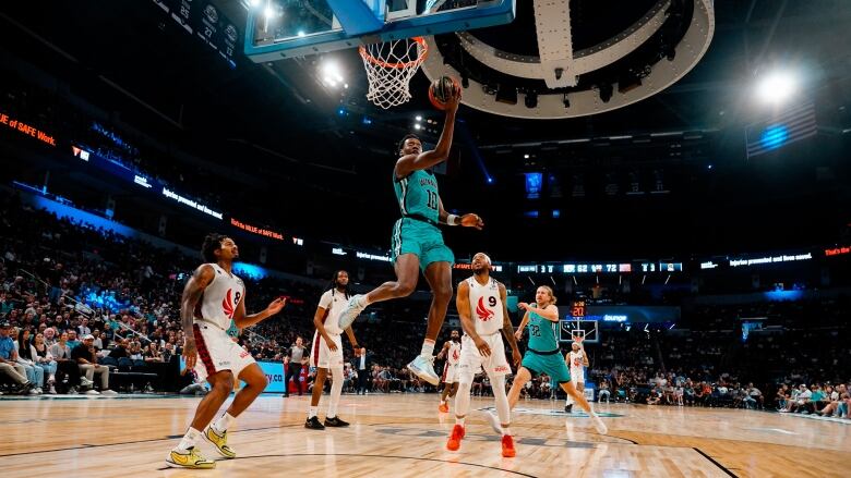 A basketball player jumps to make a basket backwards over her head.