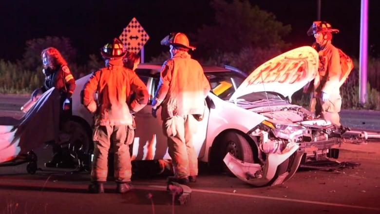 Firefighters stand in front of a damaged Toyota sedan.