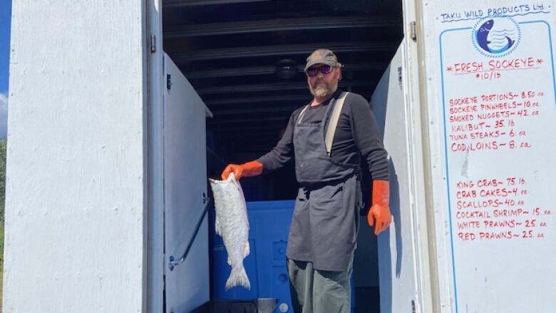 a man holds up a deheaded fish carcass out of the back of a white delivery truck