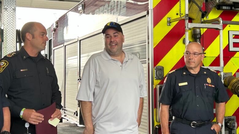 A man stands in front of a fire truck with two other men in uniforms