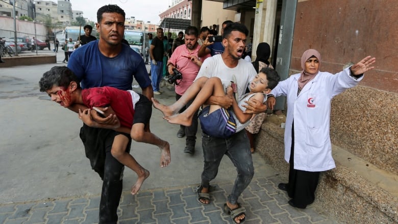 Men hold bleeding and injured children as a nurse directs them outside a hospital.