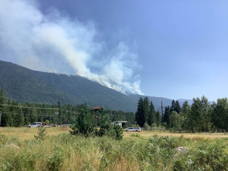 Smoke rises from the mountains, with some trailers in the foreground.