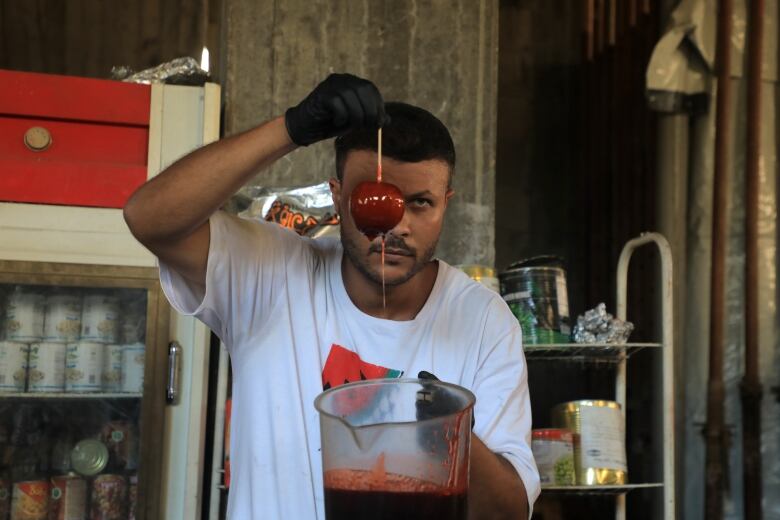 A man holds a candied apple while it drips the excess sugar coating into a bowl.