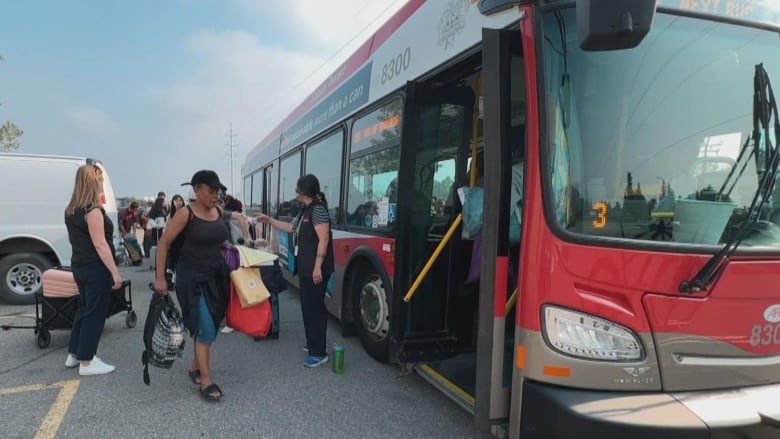 A woman with a black shirt holdng bags enters a red bus.