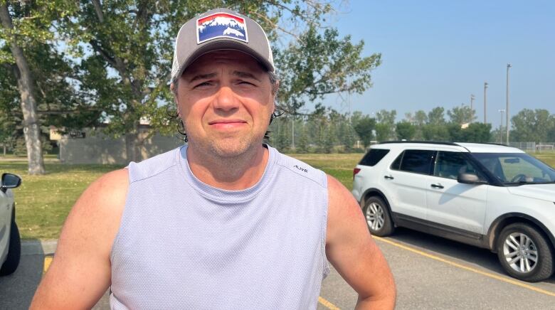 A man with a baseball cap wearing a grey shirt looks into the camera.