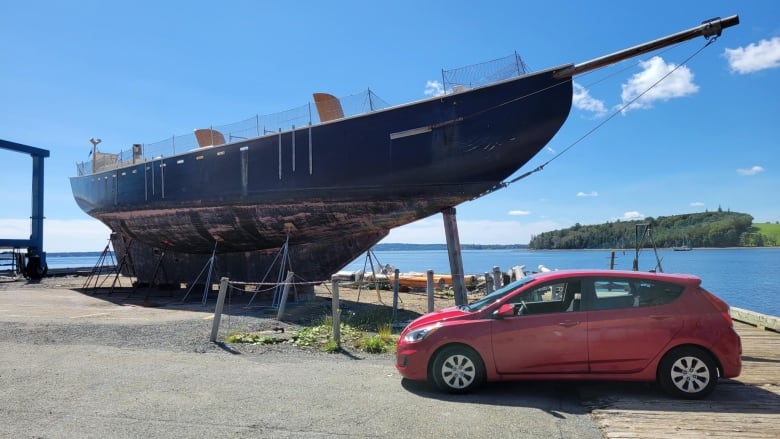 Large boat out of water beside a red car 