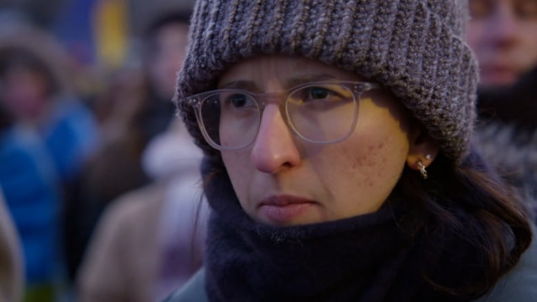 A woman wearing glasses and a knit hat stares.