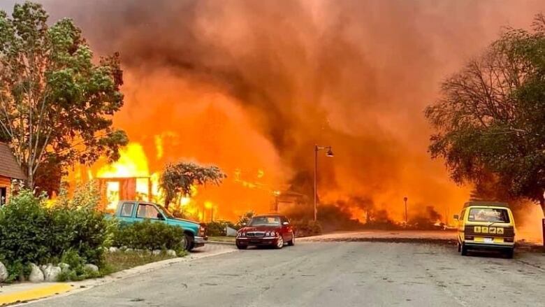 Flames whip across a street as a house burns.