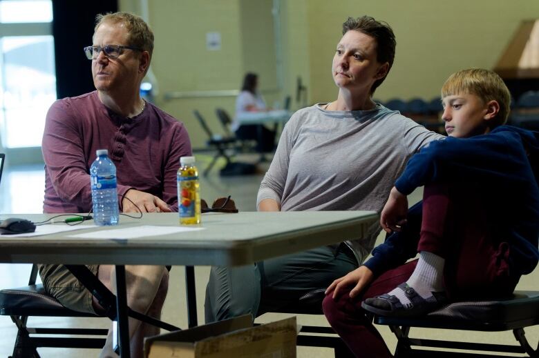 Two parents and a young boy sitting in chairs at a reception centre after they fled a wildfire in Jasper.