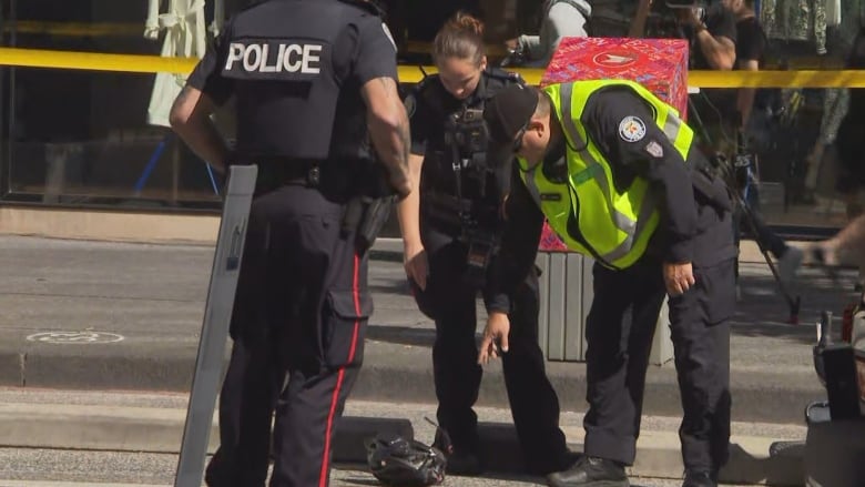 Police officers look down at a helmet lying on a roadway at an accident scene.