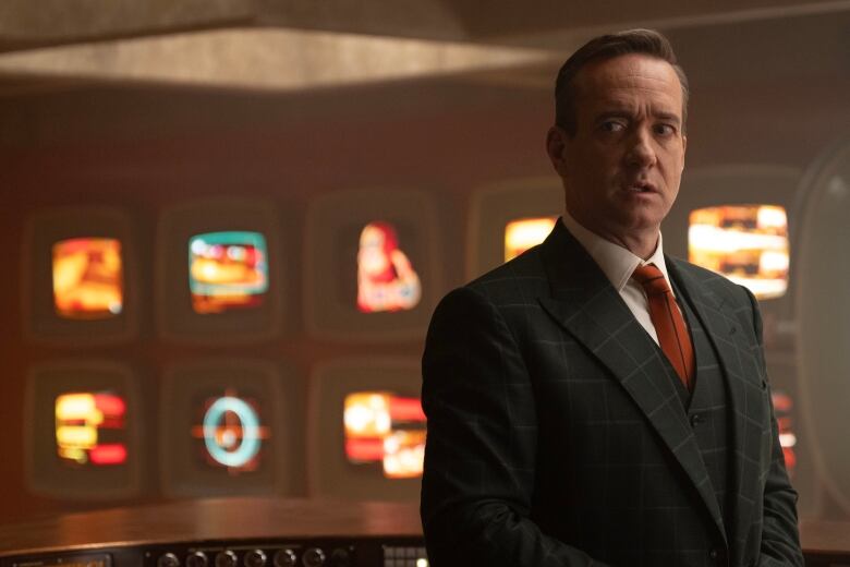 Matthew Macfadyen stands in front of a futuristic control panel. 