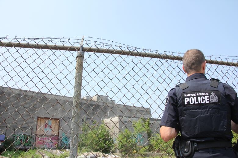 Cst. Mitchell with his back to the camera, by a fence, and looking at an abandoned building. 