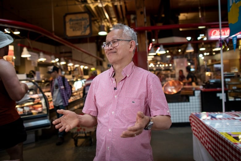 A man stands in a market smiling with his arms out. 