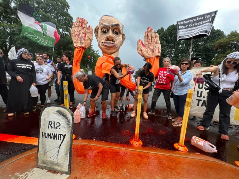 Protesters pour imitation blood on the concrete outside a government building. They are waving black, white, green and red Palestinian flags and holding a large effigy of a politician.