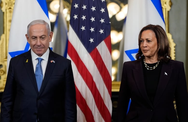 A woman and a man wearing suits stand in front of Israeli and U.S. flags. 