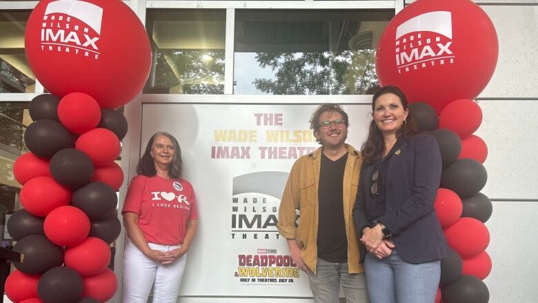 Three people stand with signs, balloons and a podium. 