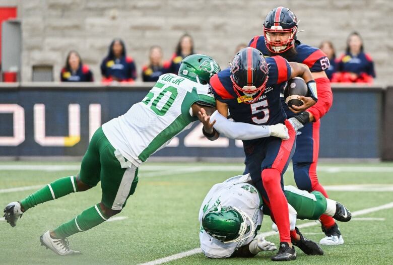 Montreal Alouettes quarterback Caleb Evans (5) is tackled by Saskatchewan Roughriders' Bryan Cox Jr. (50) during first half CFL football action in Montreal, Thursday, July 25, 2024. 