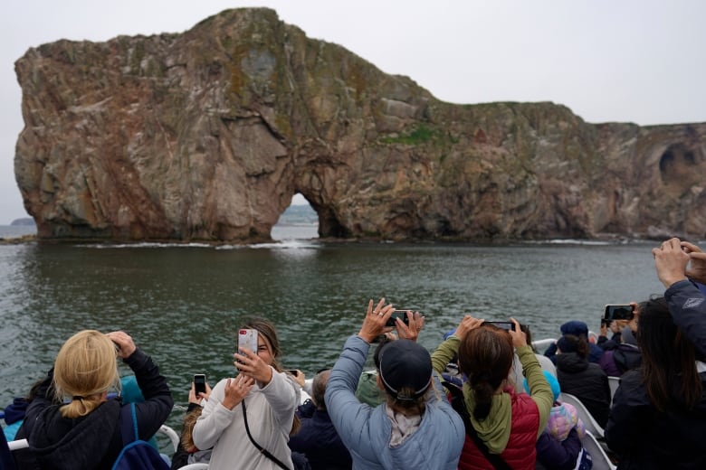 Tourists take selfies and photograph Perce Rock in Perce, Que., during a boat tour.