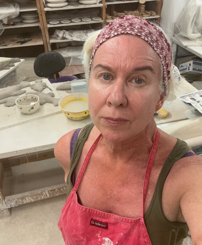 A woman in an apron with pottery pieces in the background.