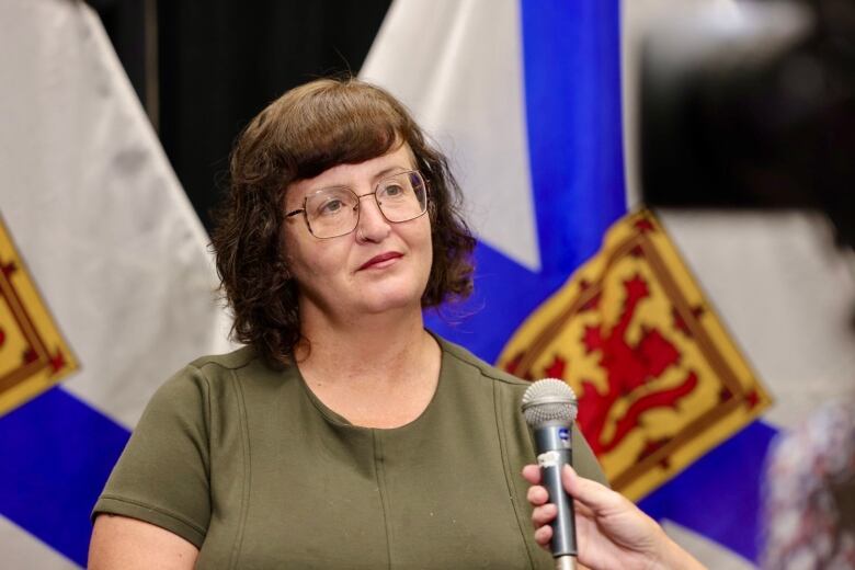 A person with brown hair and glasses stands in front of a Nova Scotia flag.