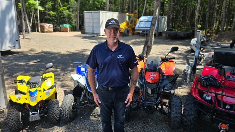 A person in a baseball cap stands in front of four off-road vehicles of varying sizes and colours.