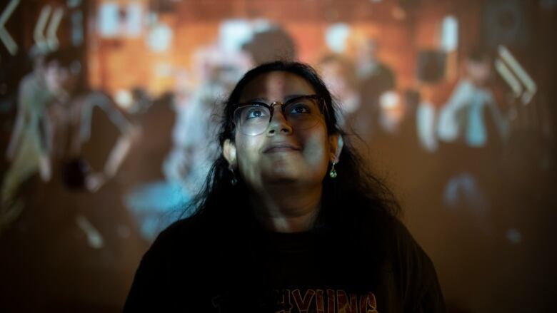 A woman smiles looking up at a performance on a projector.