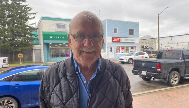 An older man standing on what appears to be a small town main street. 