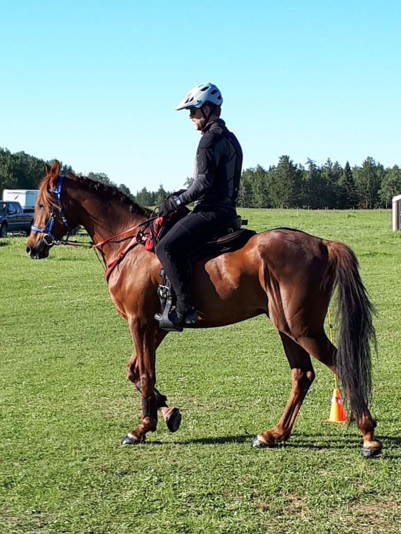 A man wearing a helmet riding a brown horse.