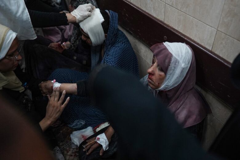 Injured people with facial bandages are seen sitting on the floor of a hospital.