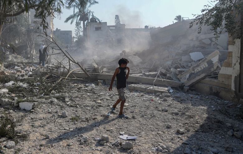 A boy walks past the rubble of a building.