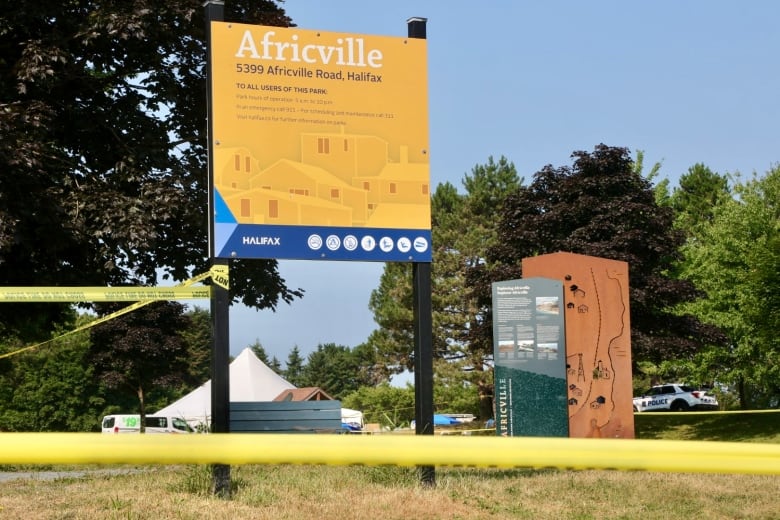 Police tape can be seen, blocking off a grassy area. Behind it is a sign for Africville