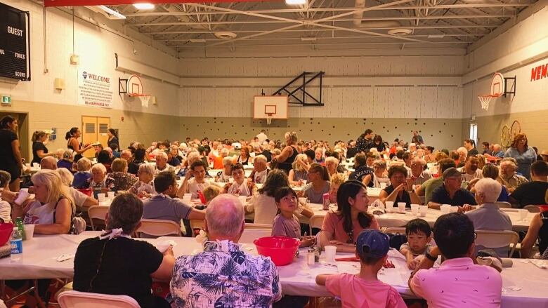 Crowd of people in gymnasium eating lobster dinners.