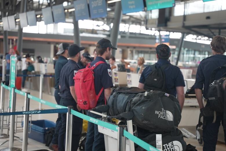 Firefighters stand in line to check their bags surrounded by luggage at the Ottawa Airport. 