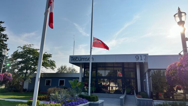 Two flags in front of a one-storey grey building that says Town of Tecumseh