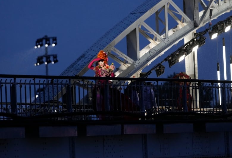 A person dressed in drag stands on a  bridge