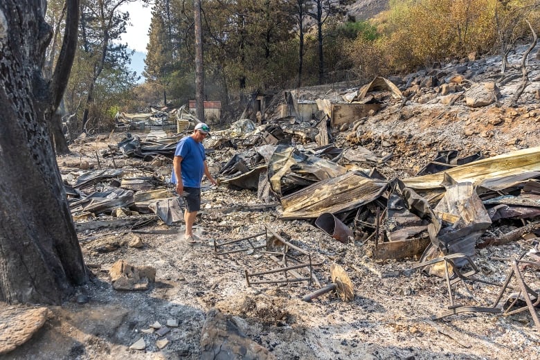 A man in a baseball cap and shorts and a tshirt is shown at a distance walking around ground that has metallic and wood debris all around.