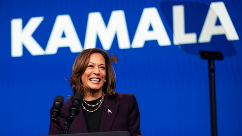 A woman in a plum-coloured suit speaks at a podium at a political rally. The name 