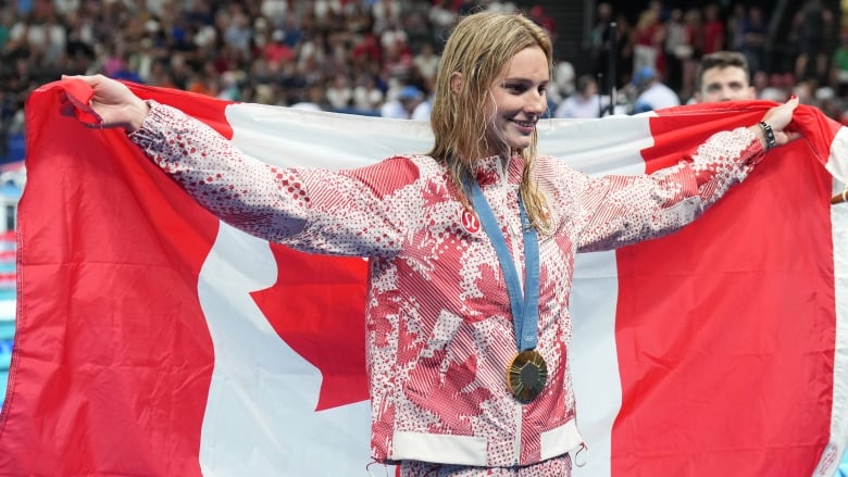 A female athlete poses for a picture with a medal around her neck and a Canadian flag behind her back.