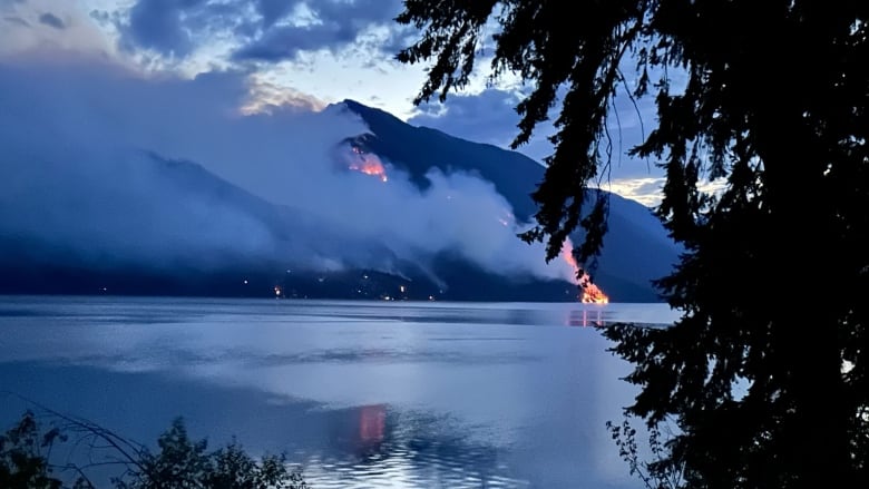 Smoke and fire are seen on the other side of a picturesque lake.