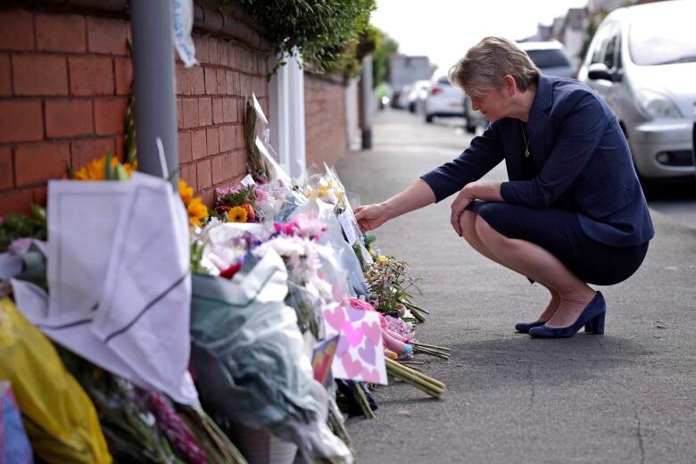 A woman kneels at bouquets of flower against a brick wall.