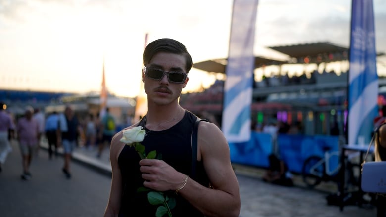 A man wearing sunglasses holds a white rose.