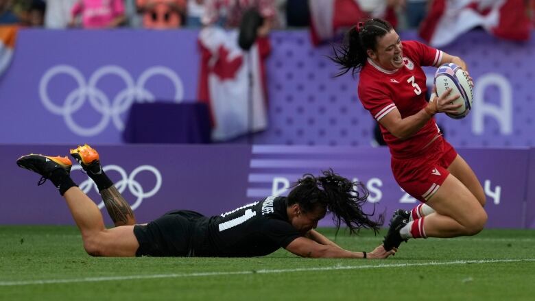 A female rugby player scores a try as she's pursued by an opposition player.