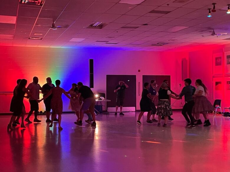 A group of people dancing in a gym with rainbow lights.